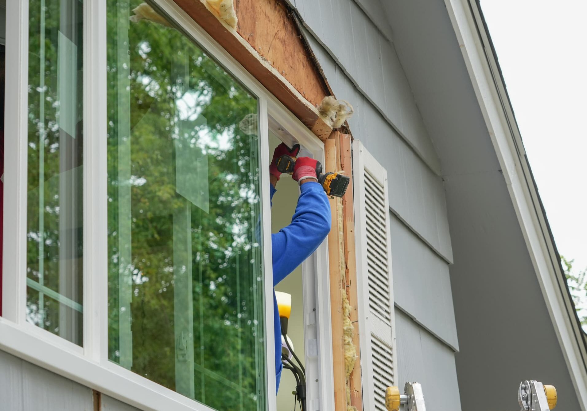 Person installing a wooden trim around a window frame on a house exterior.